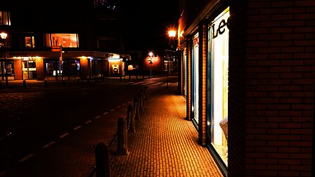 Schoutenstraat in Barneveld om middernacht. Het is een winkelstraat. Veel etages zijn verlicht. Op straat lijkt het daardoor donker