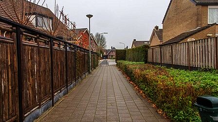 Een breed, losliggend voetpad door een woonwijk. Links van het pad zijn schuttingen, en rechts van het pad is een brede groenstrook met daarnaast schuttingen